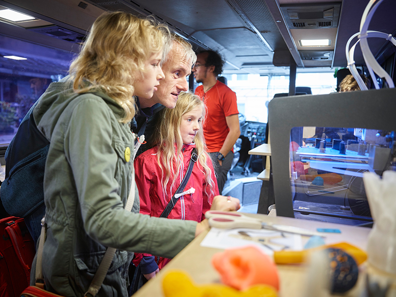 Kinder, Jugenliche und Mitarbeitende das Fabmobil beobachten im Bus einen 3D-Drucker