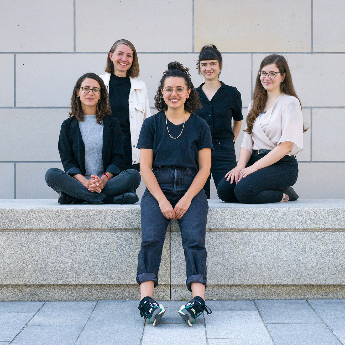 Die fünf Mitarbeiterinnen des Projekts ostklick sitzen und stehen auf einer Steinbank für ein Teamfoto.