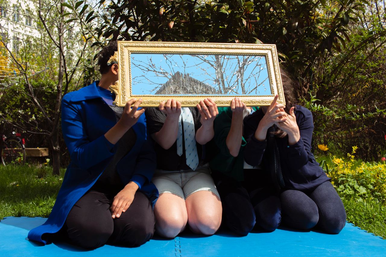 Vier Jugendliche halten sich einen goldgerahmten Spiegel vor ihre Gesichter.