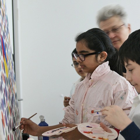 Kinder halten Farbpaletten und Pinsel in der Hand und malen auf einer Leinwand.